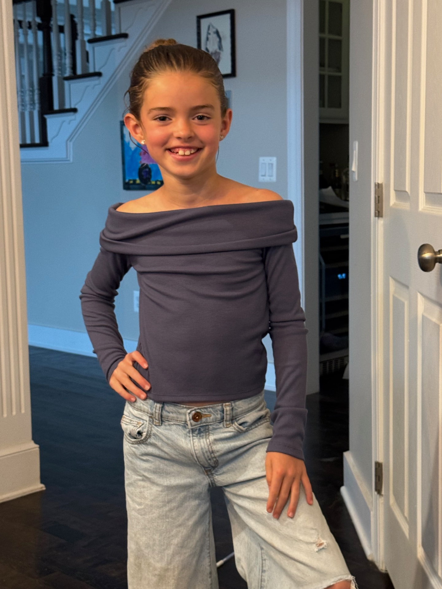 Paige smiling in a purple off-the-shoulder top and light jeans
